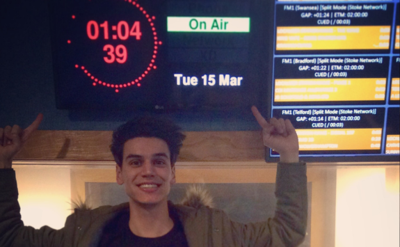 Emil smiling to camera pointing up to a TV screen which has a countdown timer on