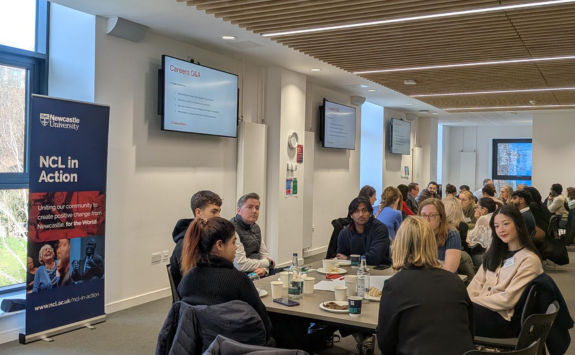 Students and professionals sat around tables with an NCL in Action banner in the background