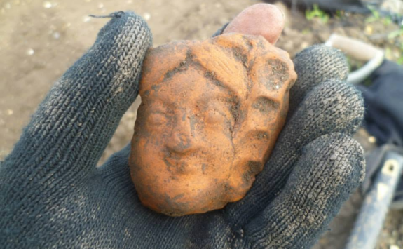 An antefix of a female face held in a gloved hand