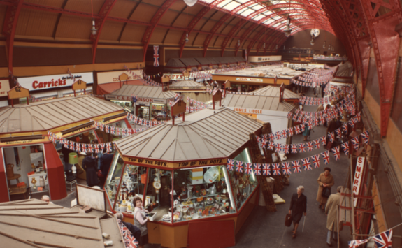 A retro photo of Grainger Market showing stalls and the canopy roof, with Union Jack bunting