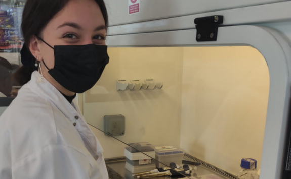 Maria wearing a face mask and white coat in a lab