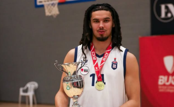 Noah stands on a basketball court holding a trophy and with a red medal ribbon round his neck