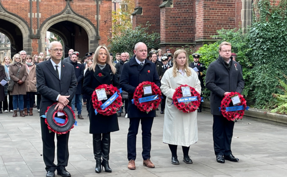 Five members of staff holding poppy wreaths in front of the Arches on campus