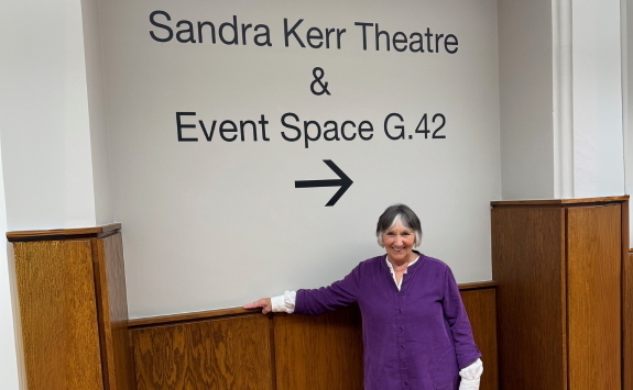 Sandra, wearing purple, stood in front of a sign saying 