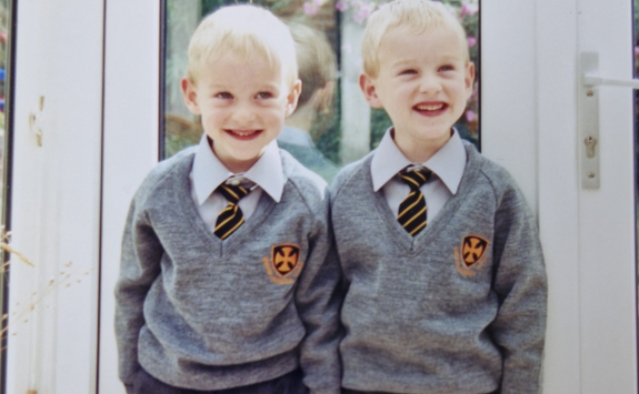 Daniel and Craig stood wearing grey school uniforms in front of french doors for their first day of school. 