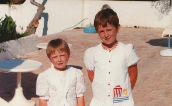 Hannah and Sarah as children on holiday, stood in a courtyard wearing white