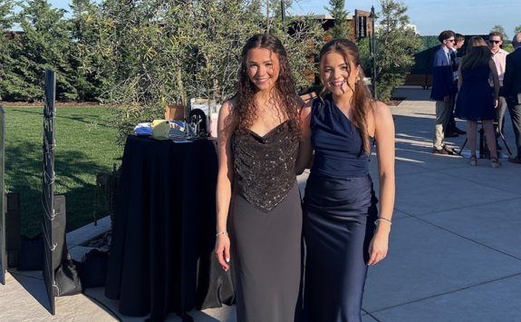 Jessica and Katie wearing formal dresses and stood outside in a manicured garden.