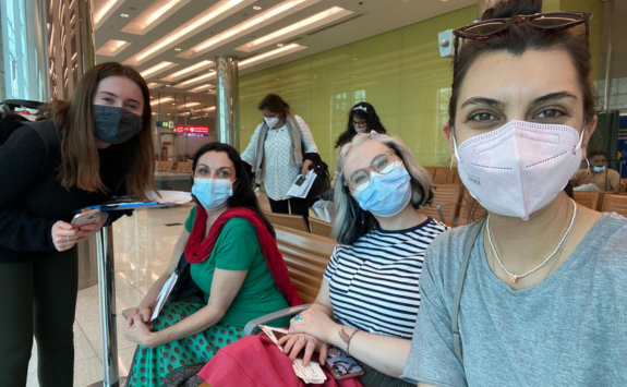 Stefani with three other people all wearing face masks while sat in an airport on the way to New Delhi