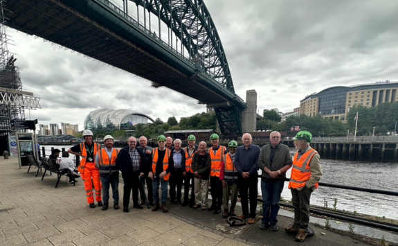 A group of engineering alumni in high vis stood under the Tyne Bridge