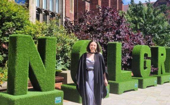 Maria proudly smiling on campus on graduation day