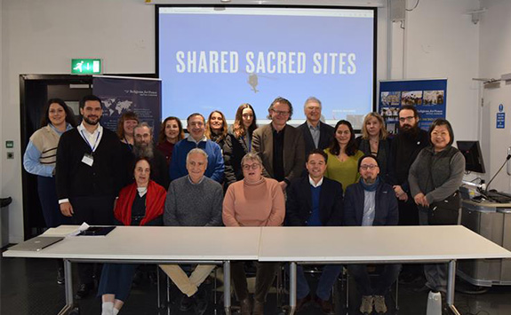 The image shows a group of around 20 people smiling at the camera. 