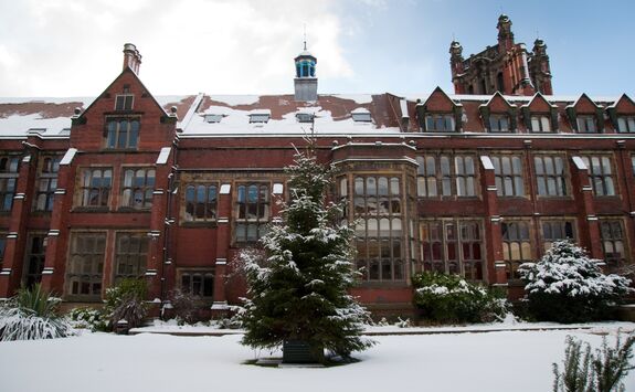 The Newcastle University quadrangle covered in snow. The building is an old, red-brick building with sandstone detailing. In front of the building is a lawn area covered in white snow.