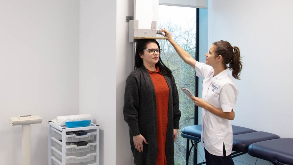 A female research participant is having her height measured as part of anthropometric assessment in a clinical research facility.