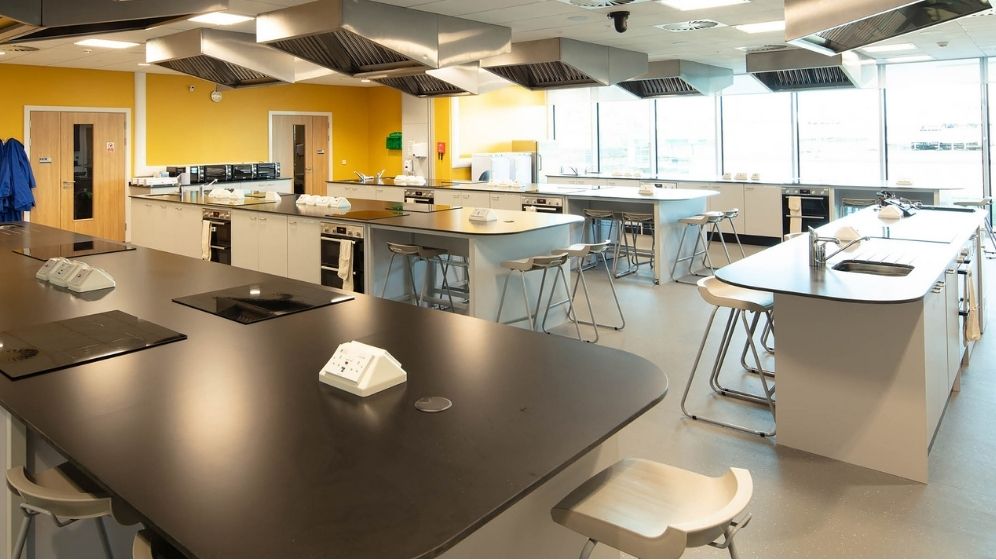 Specialist nutrition training kitchen with multiple equipped workstations, preparation areas, cooking appliances and demonstration space designed for food science, nutrition research and product development activities.