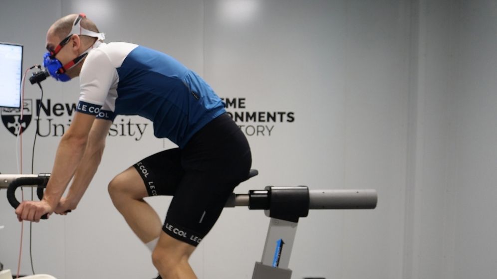 Participant using a cycle ergometer while wearing respiratory monitoring equipment during an exercise physiology assessment in Newcastle University's performance testing laboratory.
