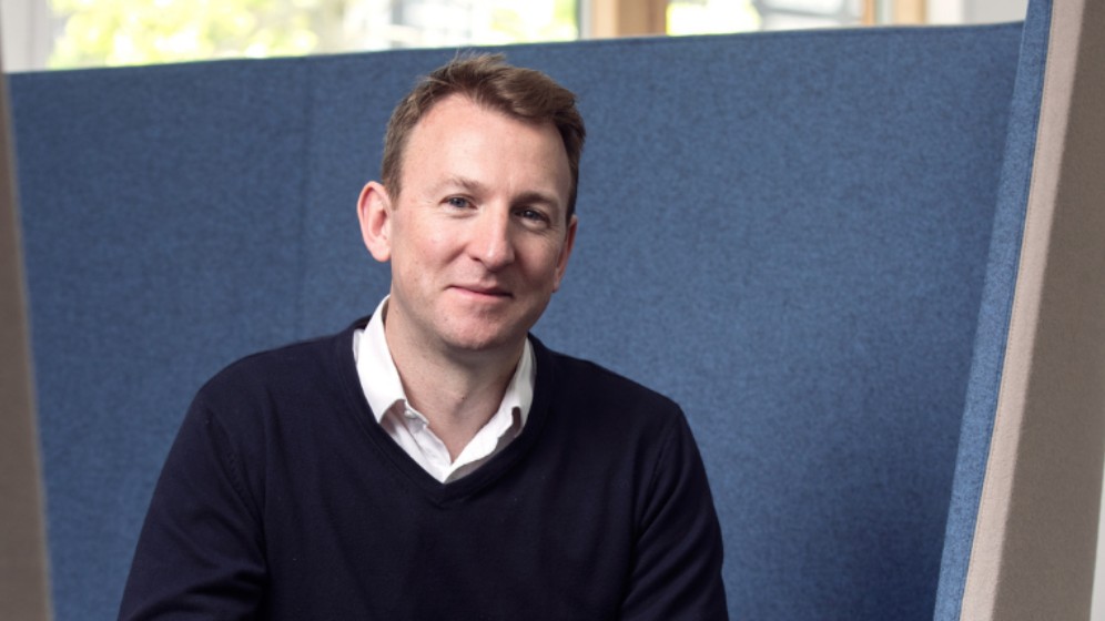 Andrew Patton, Director R&D Digital Innovation at Procter & Gamble. The picture shows a white mail sitting in a blue meeting booth. He is looking to the camera.