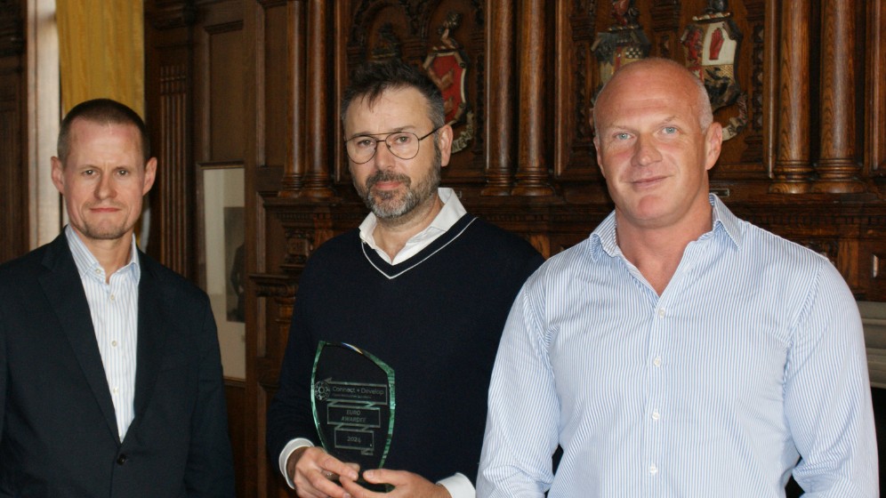 The picture shows three men standing. In the middle is Newcastle University's Professor William William Willats. He is holding a glass trophy. it is a Connect + Develop award from P&G. In the left of the image is Dr Neil Lant from P&G. And on the right is Tony McMeekin