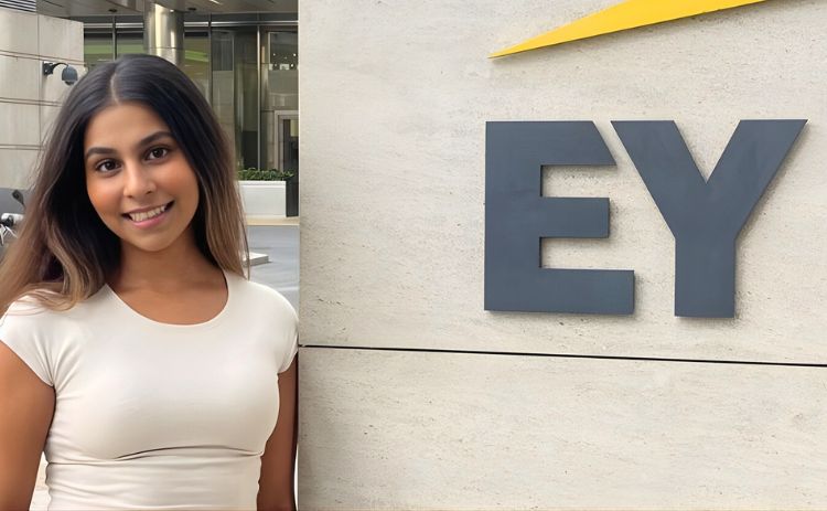 NUBS student Anushka standing outside next to a sign showing the EY logo