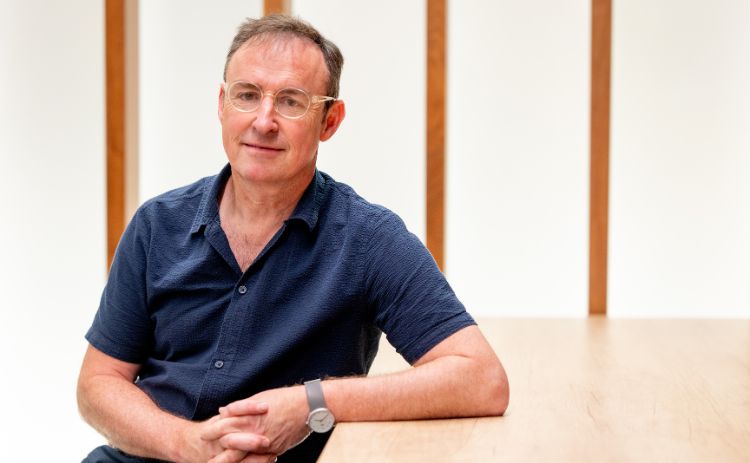 Charlie Hoult wearing dark blue shirt, sat with his left arm on a table