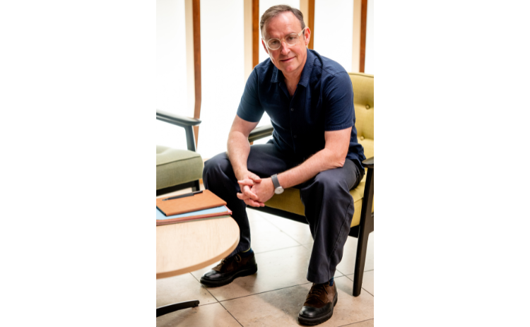 Charlie Hoult wearing dark blue shirt, sat on a yellow armchair