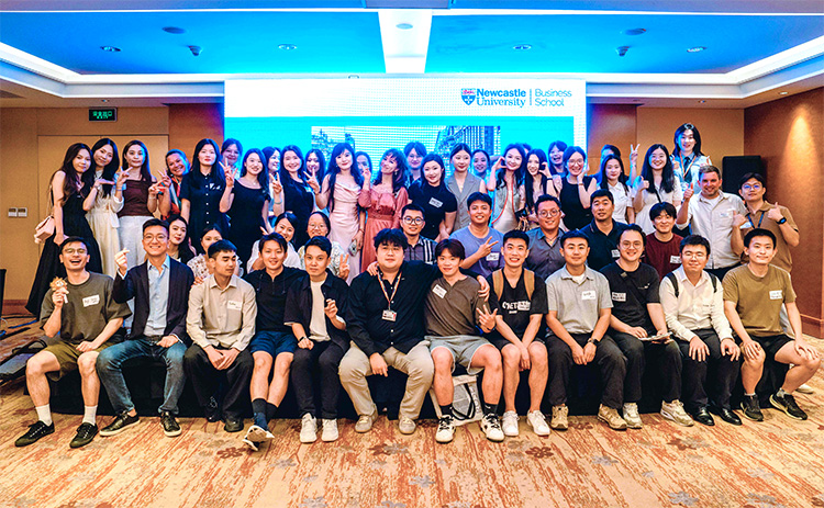 Group photo of around 50 Newcastle University Business School alumni at a community networking event in China, smiling together in front of a Business School-branded screen.