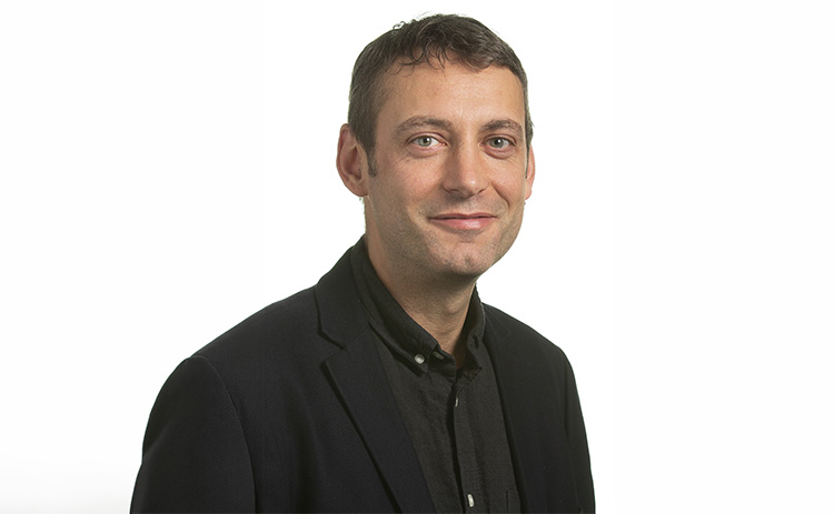 Headshot of David Lain wearing a black suit and shirt 