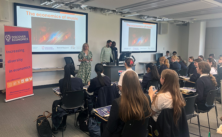 Students attend an Economics of Music session at Newcastle University, with speakers presenting at the front of the classroom.
