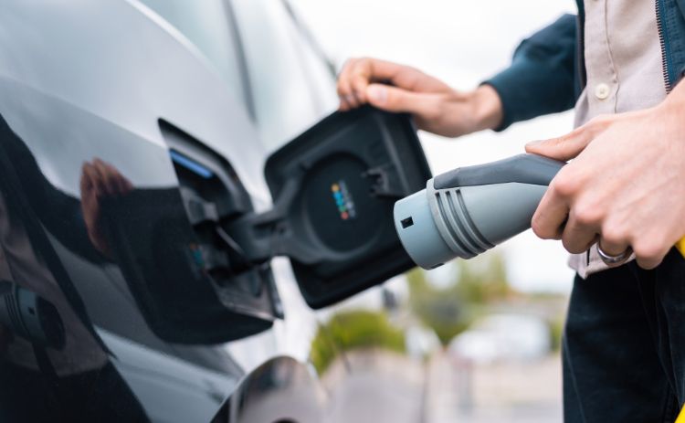 Close-up of a person plugging a charging cable into an electric car’s charging port.