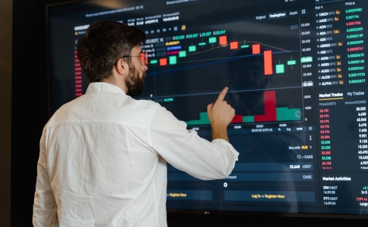 A man examines financial market data and price movements on a large digital trading screen.