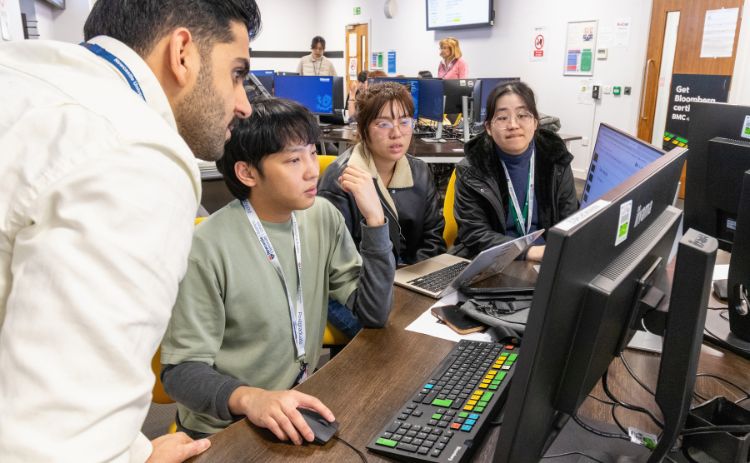 Students working together at a Bloomberg Terminal, analysing financial data on dual screens in a trading lab.