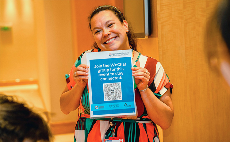 A smiling Jaclyn Wight holds up a Newcastle University Business School poster encouraging guests to join the WeChat group during the Shanghai alumni networking event.