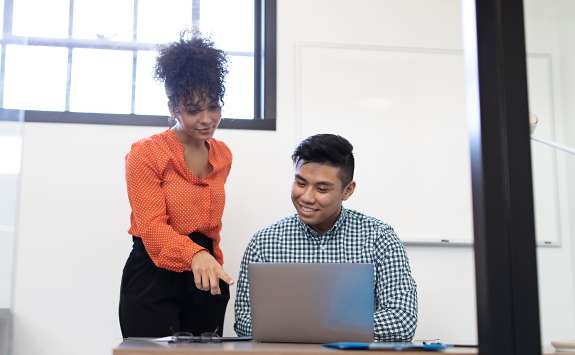A woman delivering a one-to-one mentoring session with a man sat at a laptop 