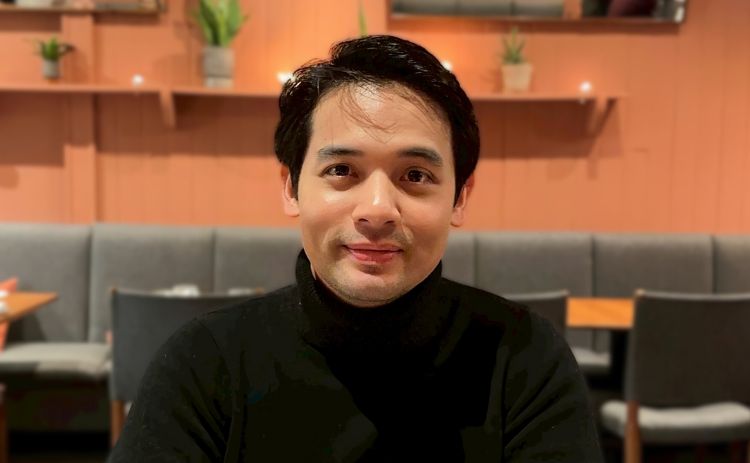 Nirat Rujimora seated at a table in a restaurant with grey sofas and wooden tables in the background
