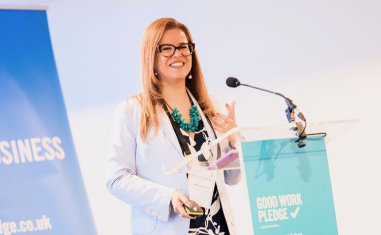 Dr Patricia Prado smiling while speaking at a podium during the Good Work Pledge event.