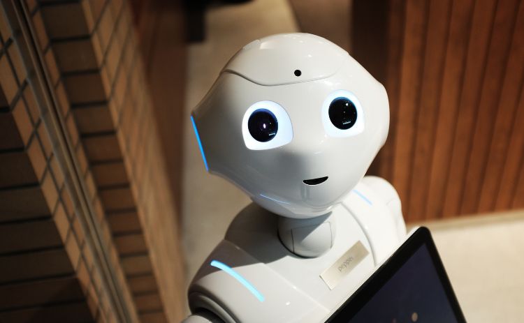 Close-up of a white humanoid robot with glowing blue eyes, standing in a building with tiled and wooden walls
