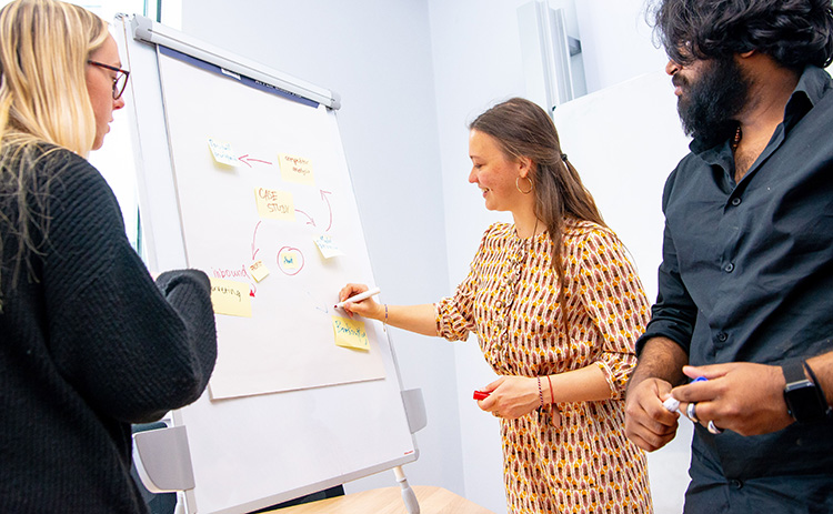 Three people collaborating, drawing diagrams on a whiteboard with sticky notes.