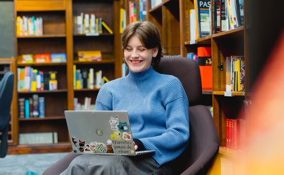A young woman smiling while looking at her laptop.