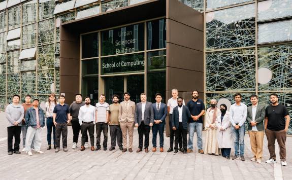 A group of researchers from Intelligent Systems pose for a group photo at the entrance of a modern building.