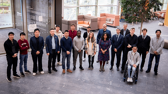 A group of researchers from Intelligent Systems pose for a group photo at the entrance of a modern building.