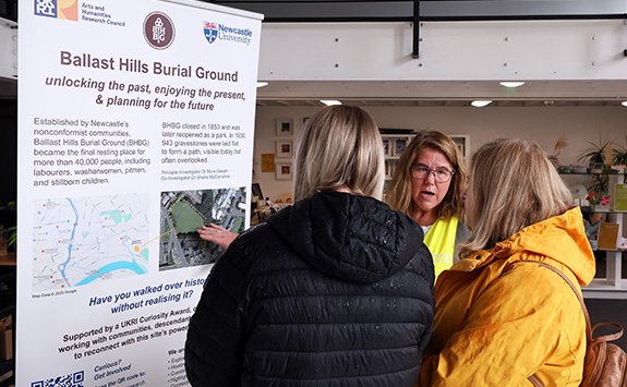 A researcher standing in front of a Ballast Hills poster chatting to members of the public