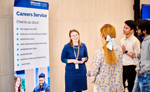 Some students and a staff member from the Careers Service chatting in front of a Careers Service banner.