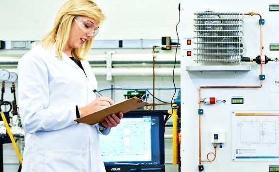 A Process Intensification student makes notes in white coat and safety glasses.