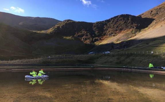 Two people in an inflatable boat carrying out water and substrate sampling at the Force Crag mine water treatment system.