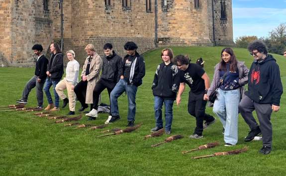 Members of the partnership with Delaware visit Alnwick castle and stand in a line with broomsticks on the floor.