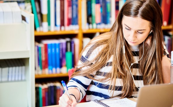Student studying in a quiet Library with books in the background.