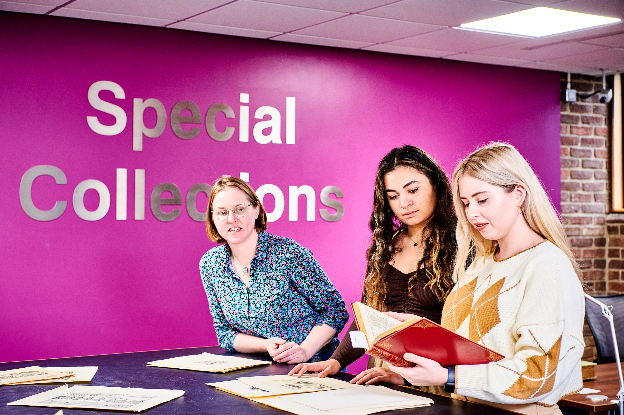 Photo of 3 people in the reading room looking at books and material laid out on a table, with 'Special Collections lettering in the background