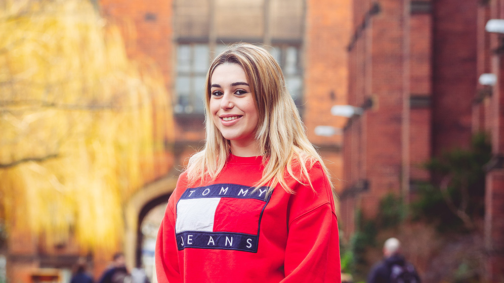 Antonia is smiling while wearing a bright red jumper bearing the 