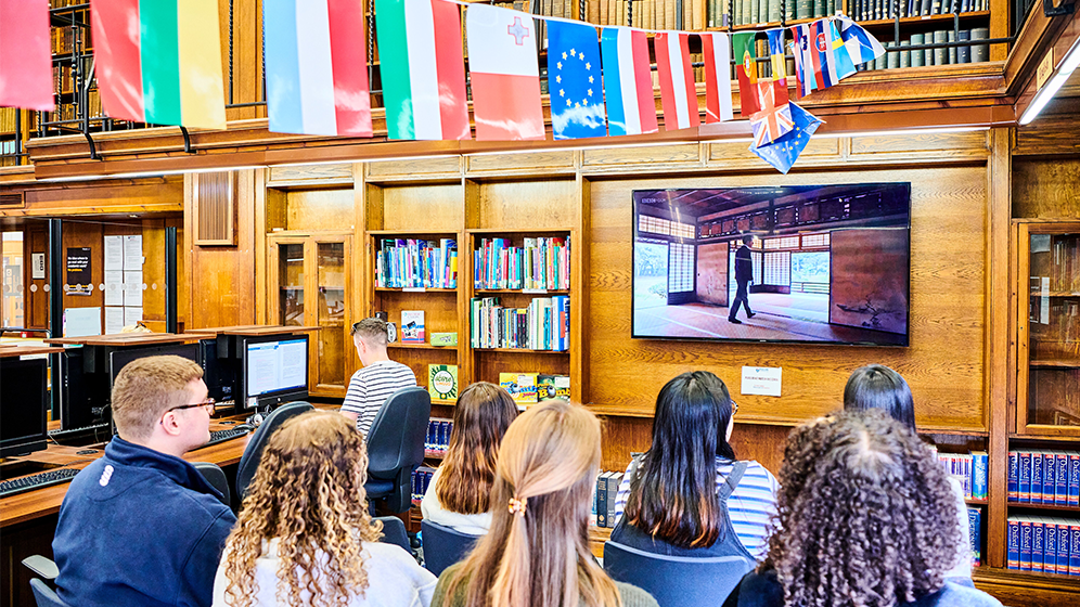 A group of students in the language resource centre watching a TV. Flags are above their heads.