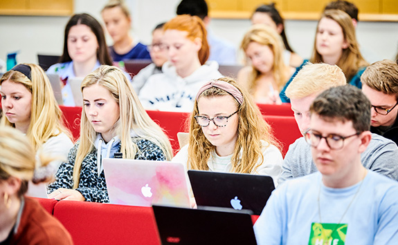 Students sitting in a lecture theatre working on their laptops. 