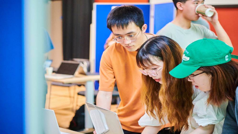 Three students working on a computer at a hackathon.